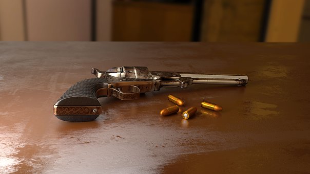 A revolver lies on a wooden surface alongside six bullet cartridges. The revolver has a textured grip and a metallic finish, with the bullets scattered randomly around it. The background is blurred in warm tones.
