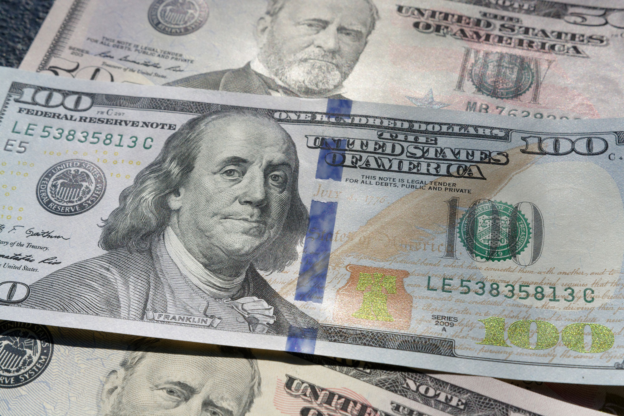 A close-up image of a 100-dollar bill featuring Benjamin Franklin is placed on top of other U.S. currency, displaying its vibrant colors and a visible security ribbon—symbolic for an alimony attorney handling intricate financial matters.