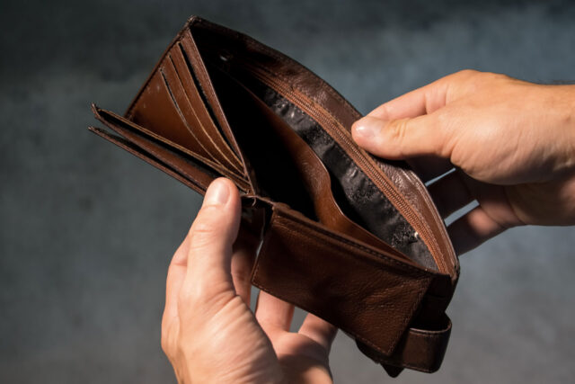 A person holds an open, empty brown leather wallet with both hands against a blurred background. Several card slots are visible, and there is no money inside, often prompting the need for bankruptcy attorneys.