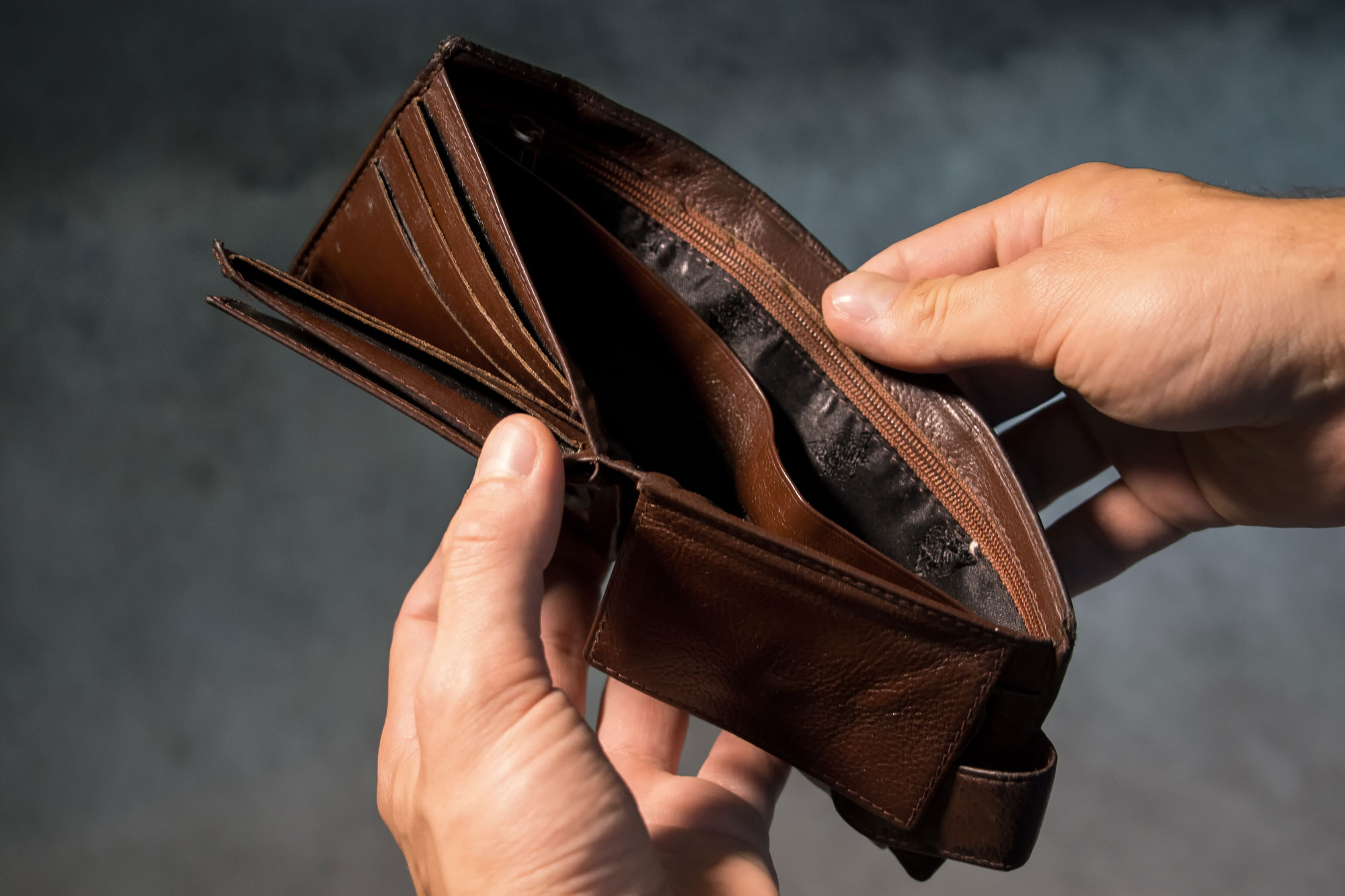 A person holds an open, empty brown leather wallet with both hands against a blurred background. Several card slots are visible, and there is no money inside, often prompting the need for bankruptcy attorneys.