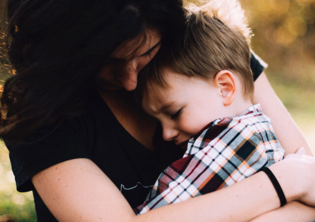 A woman with dark hair embraces a young boy in a plaid shirt. Bathed in warm, natural light, the outdoor scene feels tender and comforting. The embrace evokes the delicate bond often at the heart of child custody attorney cases.