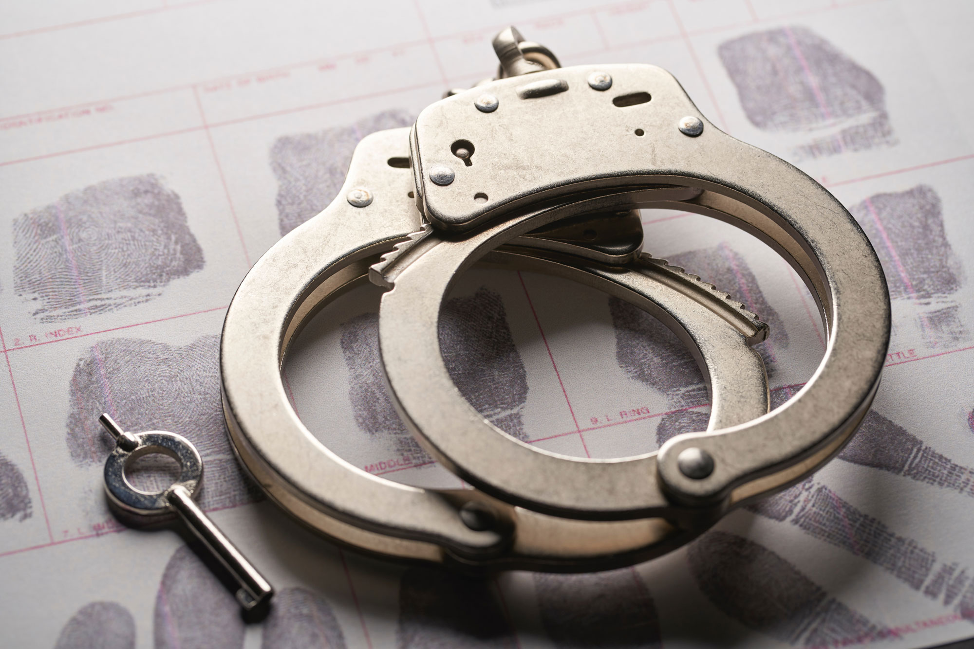 A pair of handcuffs and a small key lie on a sheet of paper featuring multiple fingerprint samples. The reflective sheen of the metal contrasts with the detailed patterns below, hinting at cases that skilled criminal defense attorneys might expertly navigate.