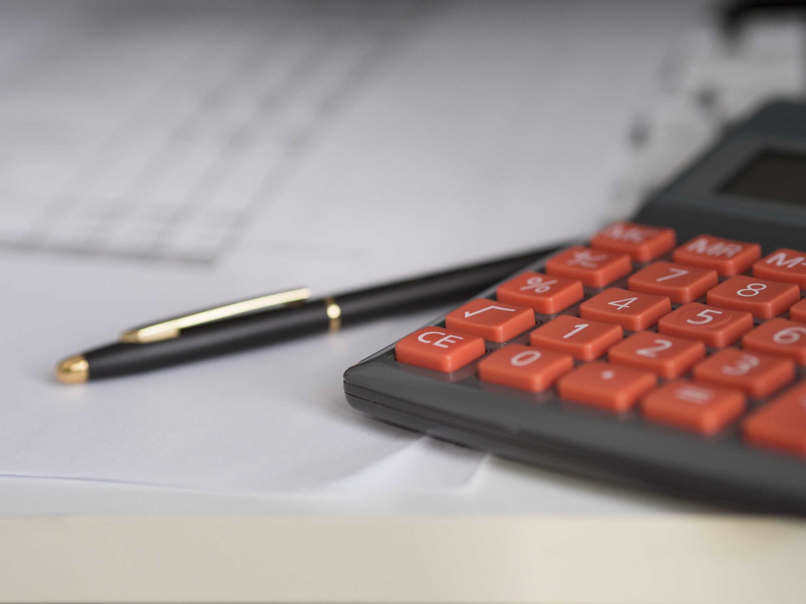 A close-up of a black and red calculator on a stack of white papers hints at commercial calculations. A black pen with gold accents rests beside it, evoking the workspace of a diligent collections attorney. The slightly blurred papers enhance the scene's professional ambiance.
