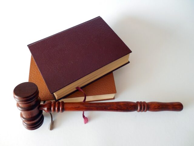 A wooden gavel lies next to two stacked brown law books on a white surface.