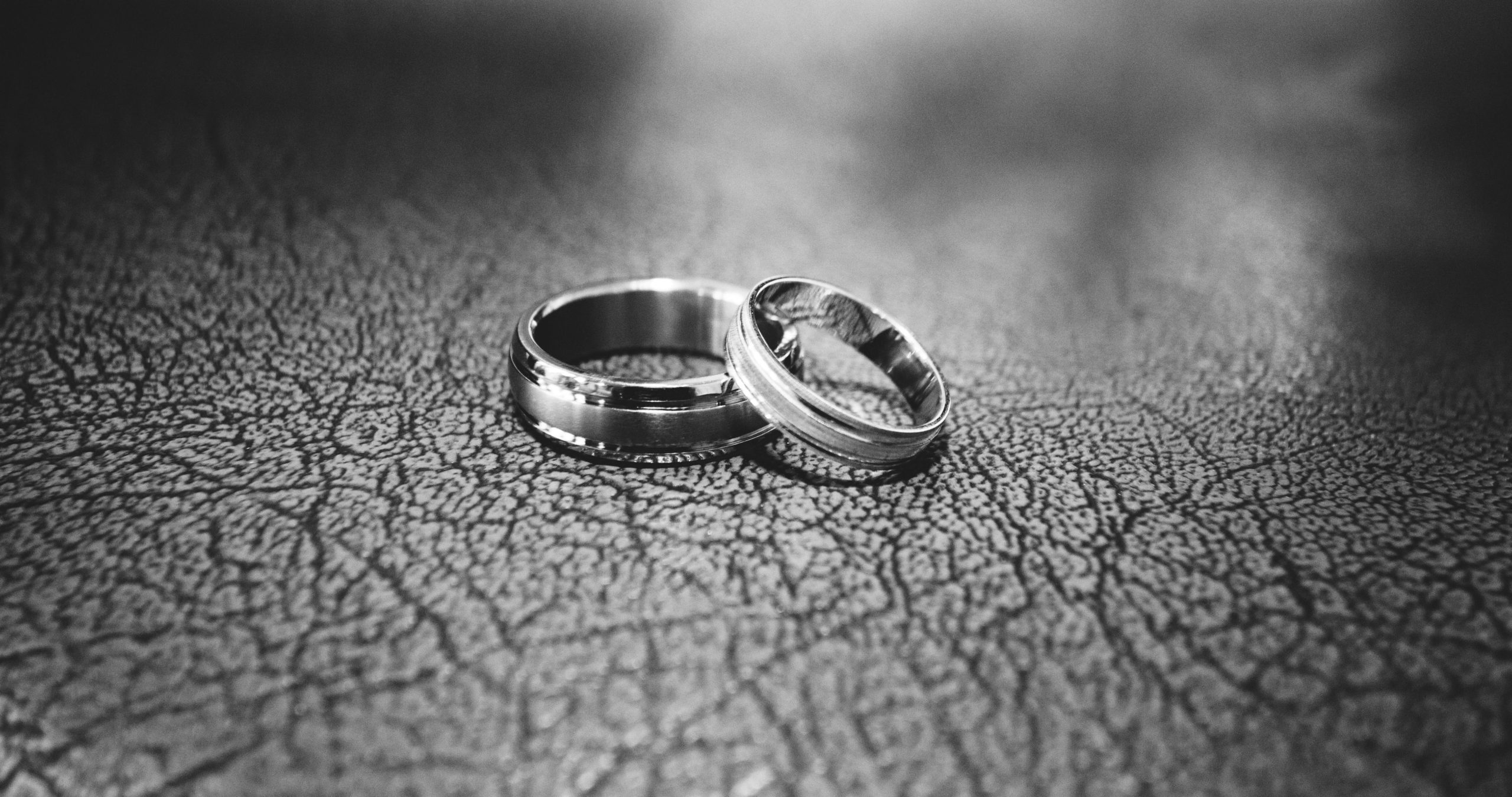 Two silver rings rest on a textured, dark surface. The rings are placed close together, with a soft focus on the background, creating a gentle, intimate atmosphere.