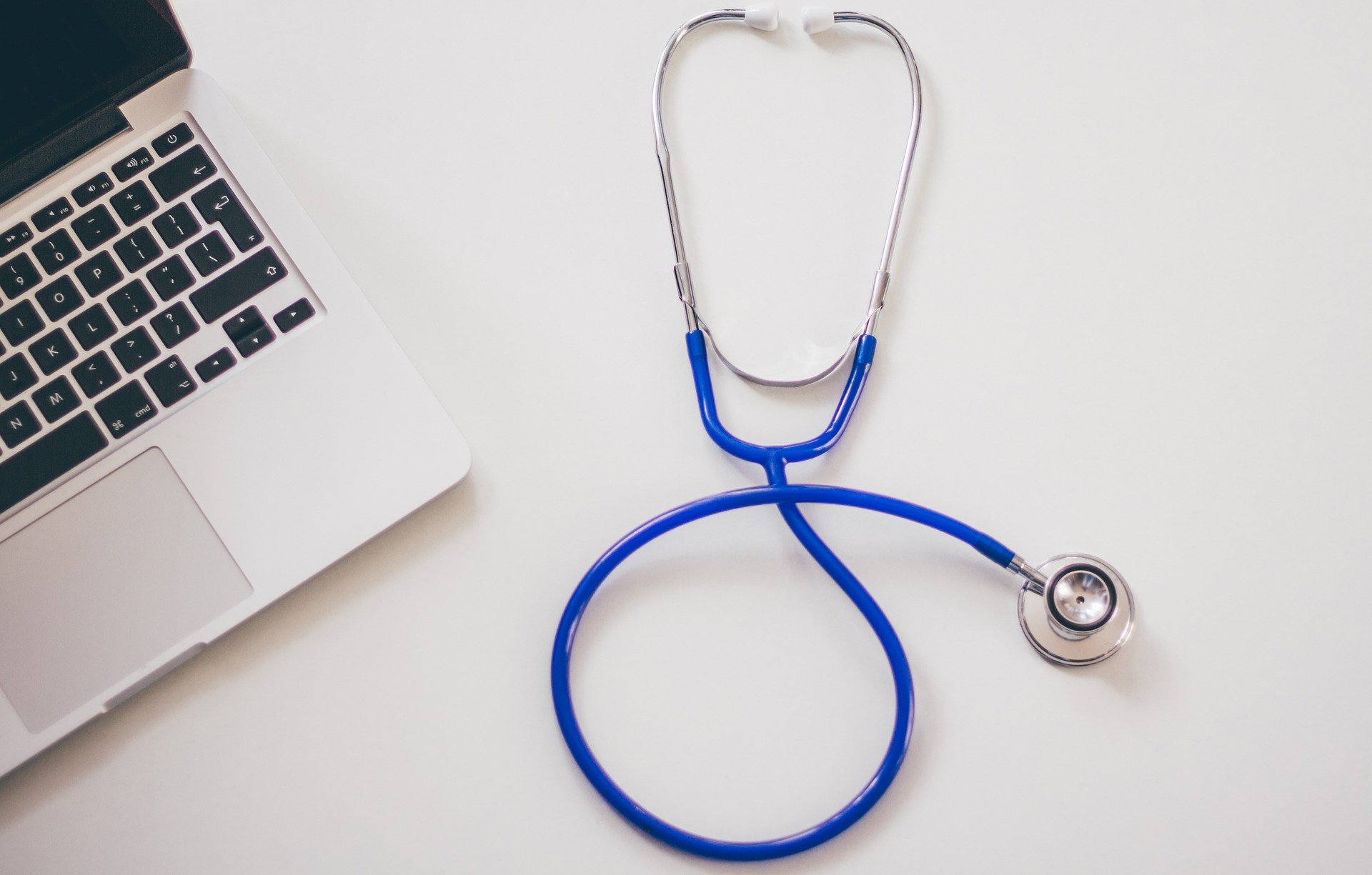 A stethoscope with a blue tube rests on a white surface beside the corner of an open laptop, evoking a medical setting. Nearby, an advance healthcare directive hints at thoughtful planning in patient care.
