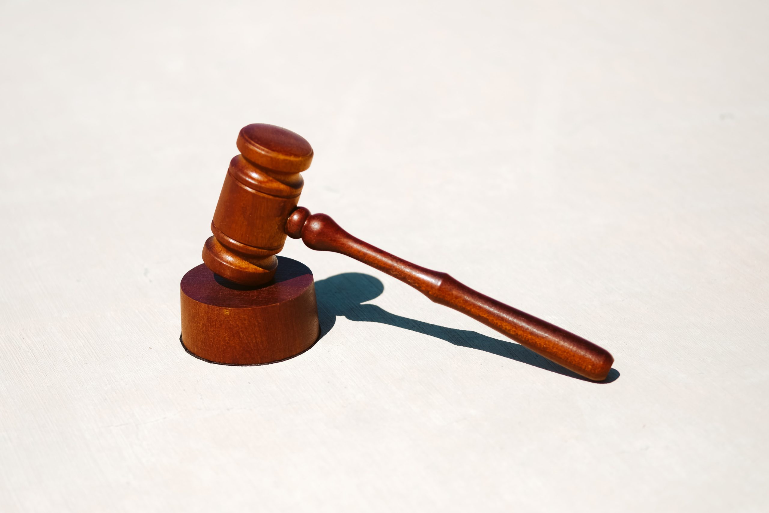 A wooden gavel, symbol of justice and powers of attorney, rests on a sound block against a plain white background, its handle angled diagonally.