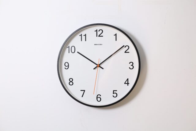 A classic round wall clock with a black frame and white face, where bold black numerals mark each hour. Black hour and minute hands, pointing to 10 and 8 respectively, are complemented by a thin red second hand at 6. This timepiece will update any room’s timeless decor.