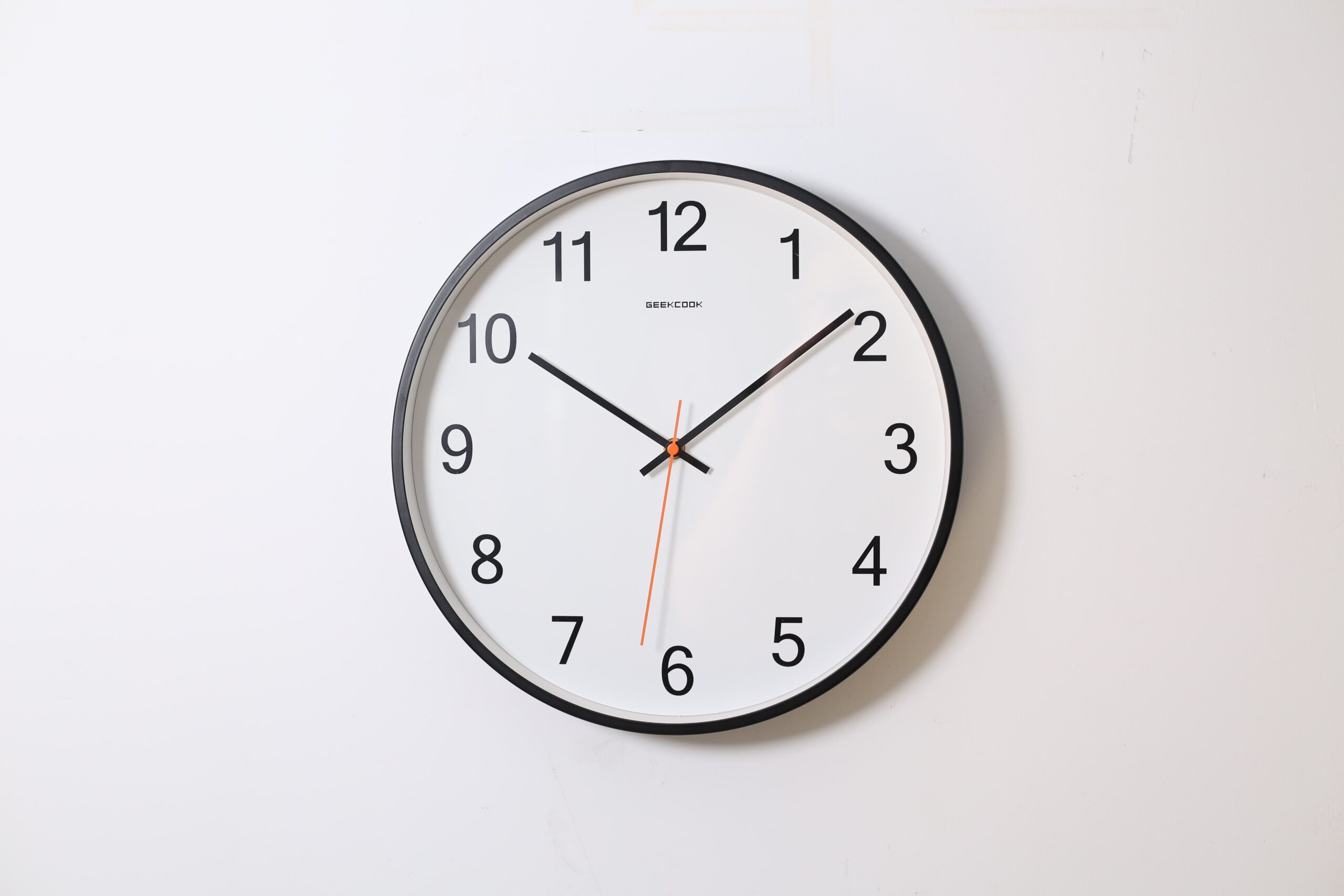 A classic round wall clock with a black frame and white face, where bold black numerals mark each hour. Black hour and minute hands, pointing to 10 and 8 respectively, are complemented by a thin red second hand at 6. This timepiece will update any room’s timeless decor.
