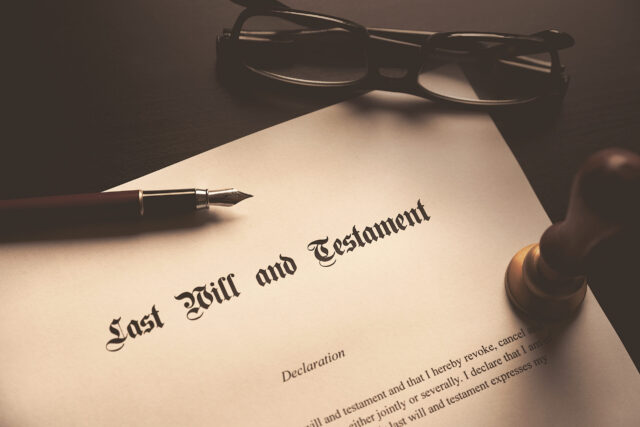 A document titled "Last Will and Testament" lies on a table. Nearby are a pair of glasses, a fountain pen, and a wax seal stamp, creating a formal and traditional setting.