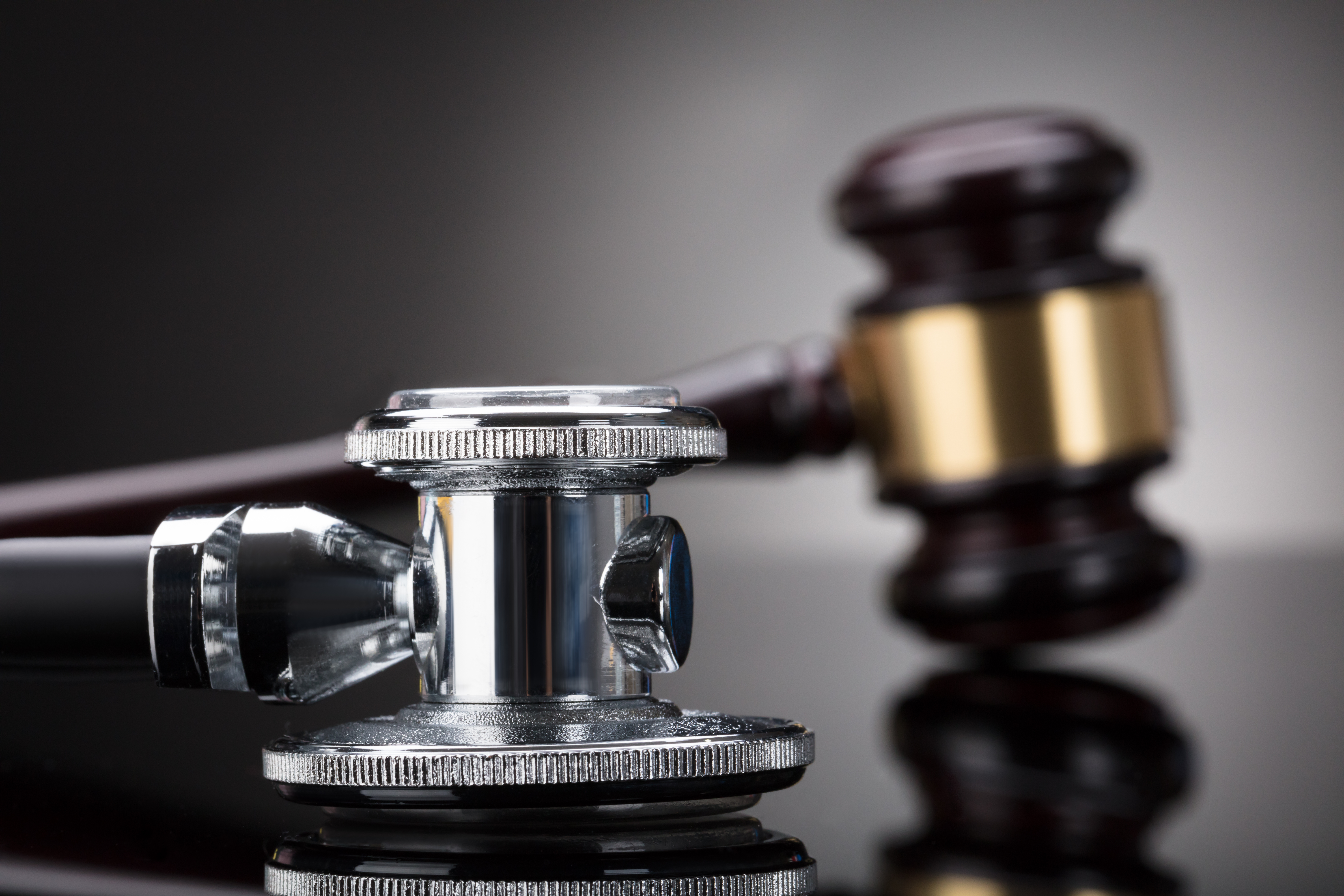 A close-up of a stethoscope placed next to a wooden judge’s gavel on a reflective surface, symbolizing the intersection of law and medicine, such as decisions involving power of attorney or healthcare proxy.