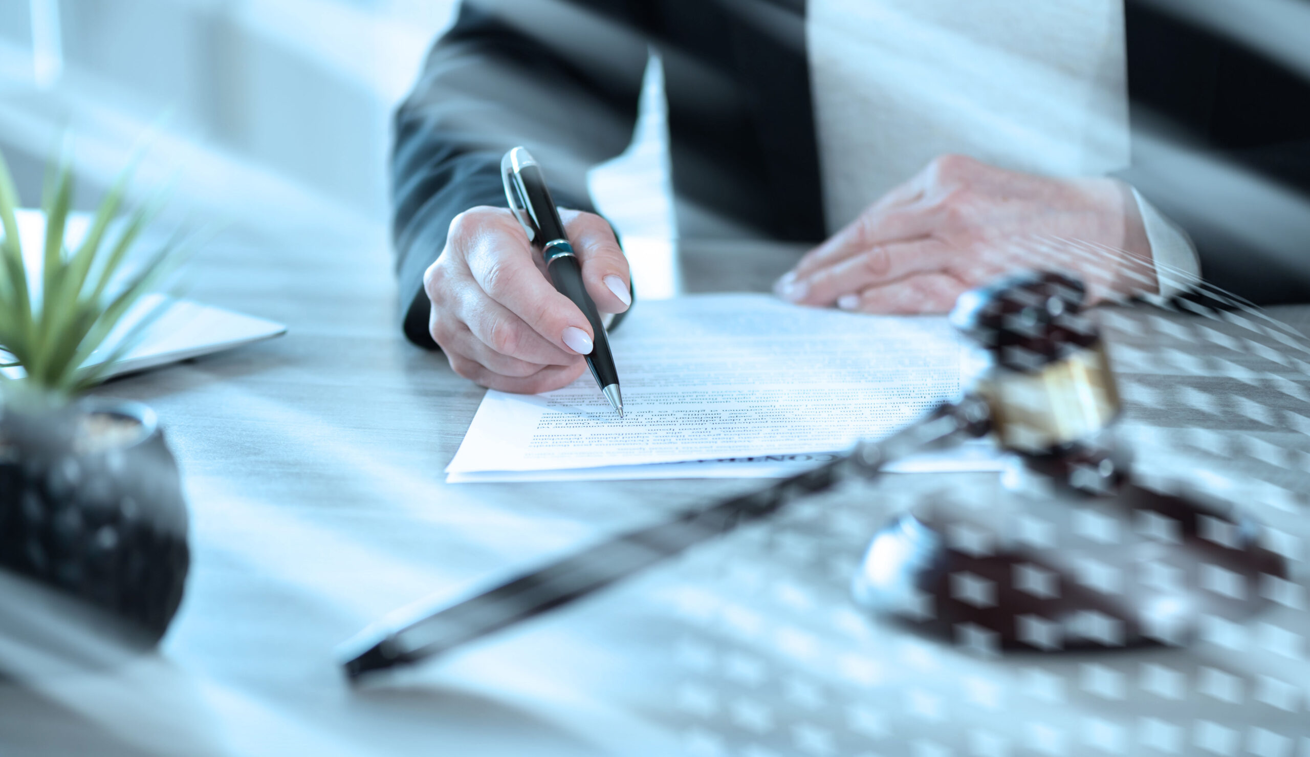A person in business attire signs a document at a desk, with a gavel and small plant nearby, suggesting a legal or professional setting where establishing guardianship may be necessary.